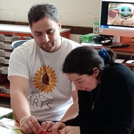 Male volunteer supporting a participant in making craft.